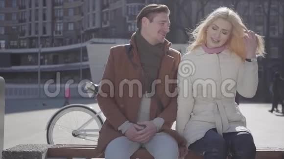英俊的男人和漂亮的金发女人穿着温暖的夹克坐在城市的街道上自行车在后面说话和微笑视频的预览图