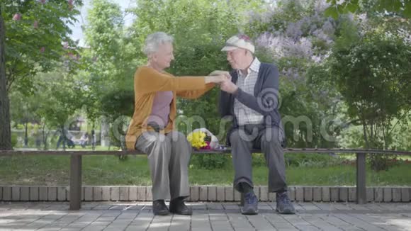肖像老妇人带着一束黄色的花坐在长凳上一位老人牵着手在公园里投标视频的预览图