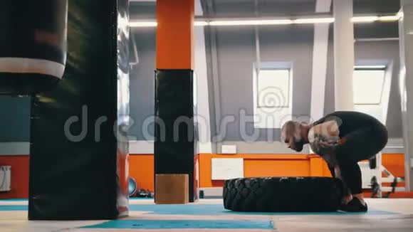 一个健美男子在健身房里一遍又一遍地翻着地板上的轮胎视频的预览图