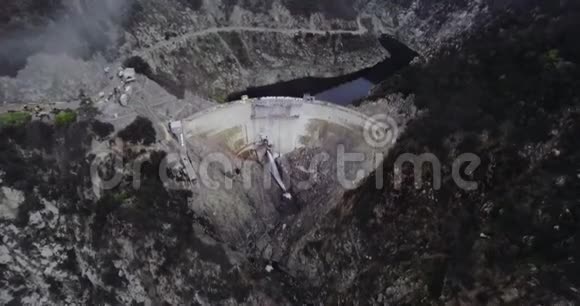 空中拍摄的一个池塘被一个大坝挡住流水在群山之间有一片森林和一条蜿蜒的道路视频的预览图