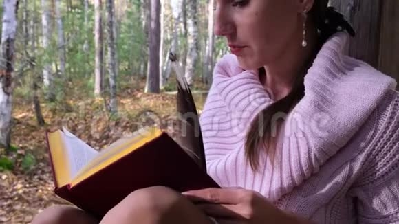 迷人的女孩正在秋天的森林里读一本书关闭视频的预览图
