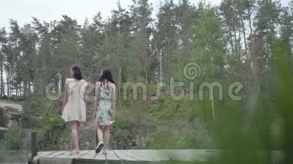 两个可爱的年轻女人穿着夏装站在岩石的顶部看着大自然漂亮的女孩走出去视频的预览图