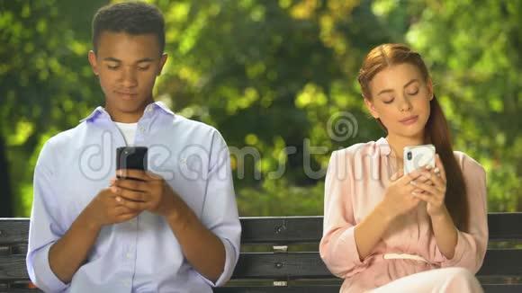 男女青少年坐在长凳上在智能手机上聊天问题视频的预览图