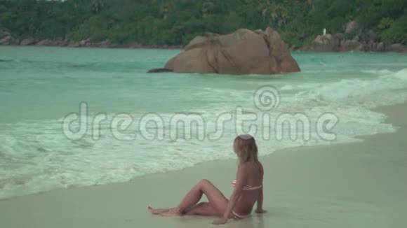塞舌尔普拉斯林岛可爱的晒黑的女人苗条的身体坐在沙子上穿着蓝色干净的水女士在休息视频的预览图