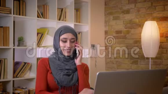年轻迷人的穆斯林女商人戴着头巾打字时随意在电话上交谈视频的预览图