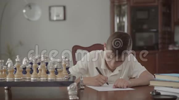 一个可爱体贴的家伙坐在桌子上在一张纸上写东西的肖像视频的预览图