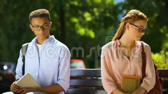 戴眼镜的胆小学生试图结识朋友坐在公园的长凳上视频的预览图