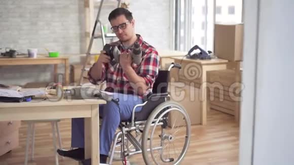 残疾人轮椅上有电钻的青年从事修理工作视频的预览图