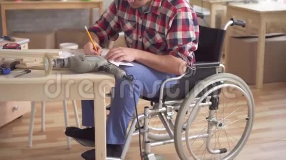 轮椅上的一名青年残疾人用电钻组装家具的肖像视频的预览图