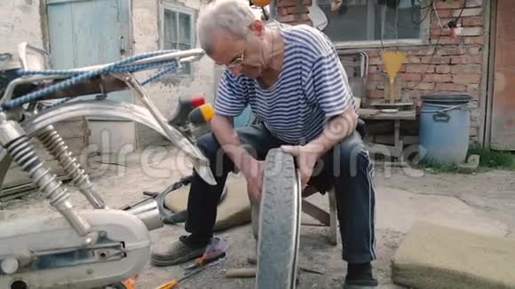 一位老人在村里的院子里修理自行车老人修理摩托车的轮子视频的预览图