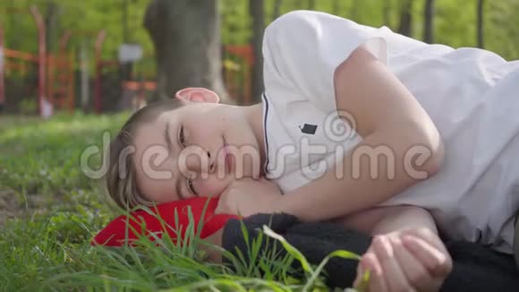 春天公园里一个可爱的男孩躺在绿草上的肖像户外娱乐活动视频的预览图