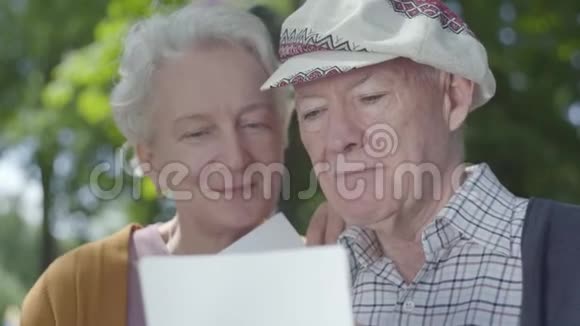 特写肖像可爱的成人夫妇看着老照片回忆着坐在公园长凳上的快乐时刻视频的预览图
