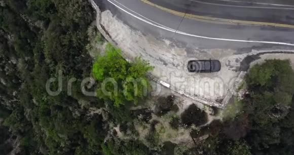 一辆黑色汽车在路边靠近山坡上的绿色灌木丛视频的预览图