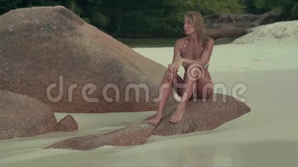塞舌尔普拉斯林岛穿着泳装的黝黑美丽的女人苗条的身体坐在蓝色的大石头上视频的预览图