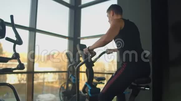 年轻的积极分子在健身房里用运动鞋旋转一辆空中自行车男子骑自行车训练视频的预览图