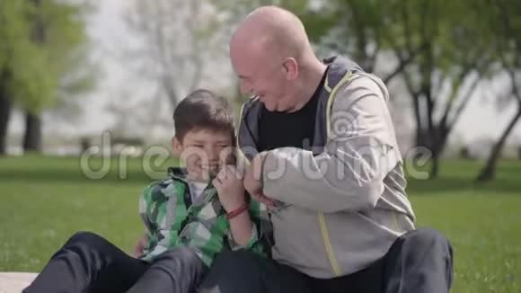 老人和孙子坐在公园的毯子上逗着小男孩孩子在笑休闲视频的预览图