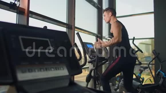肖像健身男子在健身俱乐部椭圆交叉教练训练前热身近距离男性训练视频的预览图