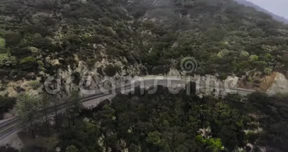 在雾蒙蒙的云层下山坡上有一片黑森林的公路转弯处的空中拍摄视频的预览图