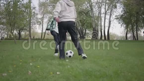 小男孩和他的父亲或祖父在公园里踢足球或踢足球那个孩子想捡球视频的预览图