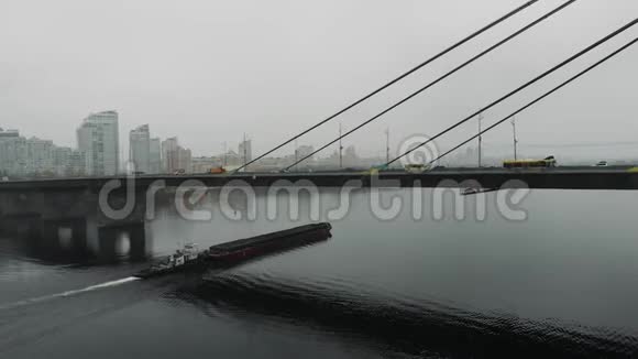 在市中心的工业烟雾中用钢缆连接的混凝土大桥一艘满载沙子的大驳船在宽阔的小溪下漂浮视频的预览图