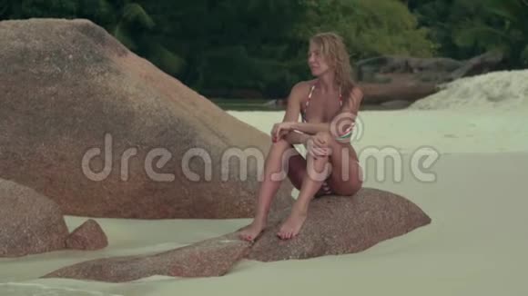 塞舌尔普拉斯林岛穿着泳装的黝黑美丽的女人苗条的身体坐在蓝色的大石头上视频的预览图