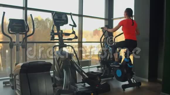 年轻活跃的女人在健身房里用运动鞋旋转一辆空中自行车女子空中自行车训练视频的预览图