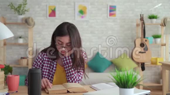漂亮的亚洲女孩戴着眼镜长发在客厅里现代人看书喜欢语音助手视频的预览图