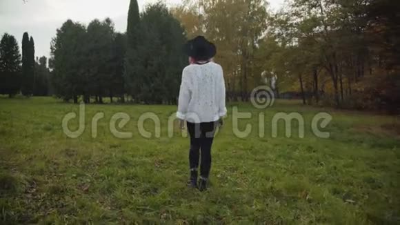 戴黑帽子的女孩在公园的草坪上散步视频的预览图