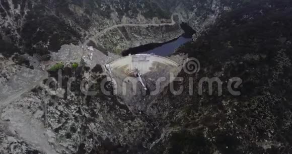 无人机用一股水流击打了一座水坝这股水流阻挡了山上的一个池塘那里有一片漆黑的森林和蜿蜒的道路视频的预览图