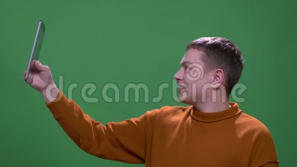 在平板电脑上播放视频的年轻白种人男性特写镜头背景是绿色的视频的预览图