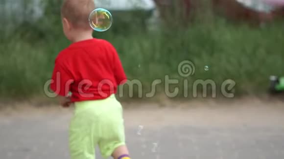 可爱的男孩在慢动作模糊的汽车背景上捕捉肥皂泡视频的预览图