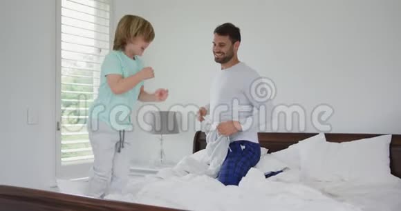 在舒适的家里父亲帮助儿子在卧室的床上穿衣服视频的预览图