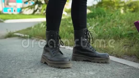 夏天穿着黑色皮靴的女性腿站在沥青路上穿着皮鞋走在绿草上的女孩视频的预览图