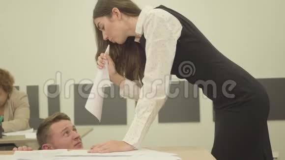 肖像紧张愤怒的年轻女子把纸折成角对坐在桌子下面的男人大喊大叫视频的预览图
