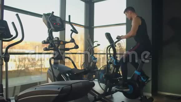 年轻的积极分子在健身房里用运动鞋旋转一辆空中自行车男子骑自行车训练视频的预览图