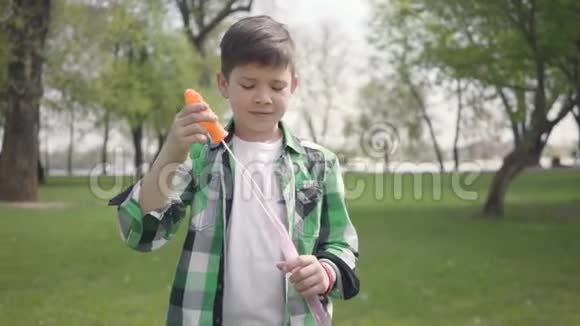 肖像可爱的小男孩穿着格子衬衫把汤泡泡吹得很近这孩子在户外玩得很开心视频的预览图