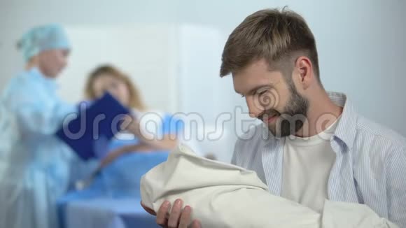 幸福的父亲抱着新生儿在护士解释妻子产后护理视频的预览图