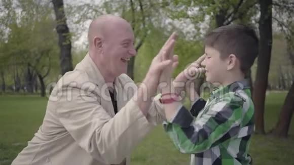 积极的爷爷和可爱的孙子穿着格子衬衫高五在公园里都笑了世代概念视频的预览图