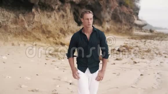 孤独的男人穿着白色的裤子和黑色的衬衫沿着沙滩散步视频的预览图