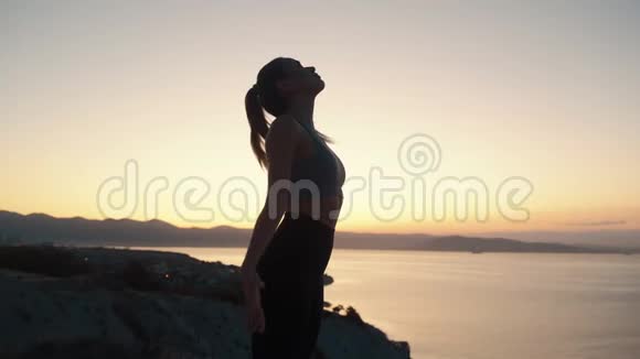 美丽的女人练习瑜伽在日出时用海景冥想慢动作视频的预览图