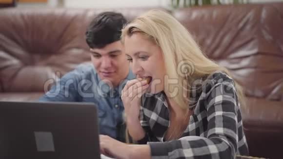 肖像年轻夫妇坐在家里的笔记本前英俊的黑发男人和可爱的金发女人视频的预览图