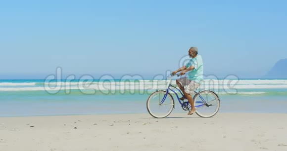 在阳光4k的海滩上骑自行车的活跃的非裔美国老人的侧景视频的预览图