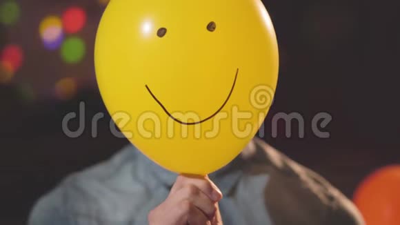 一个自信的年轻人戴着生日帽的特写肖像摘下一个画着滑稽脸的气球看着视频的预览图
