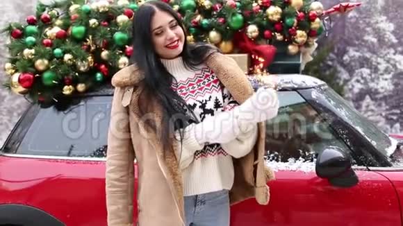 漂亮的小女孩在装饰着圣诞树的红色汽车旁玩着火花视频的预览图