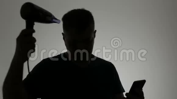 一个男人的剪影他把吹风机擦干看着智能手机的屏幕视频的预览图