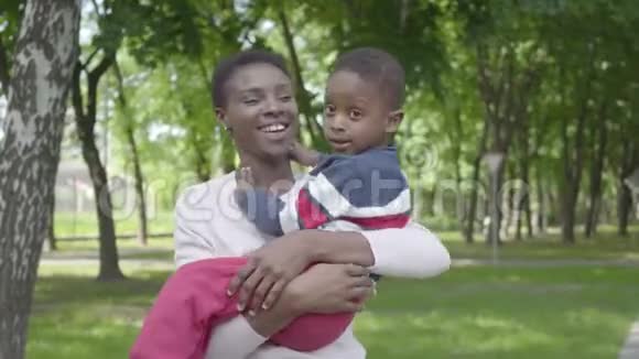 美丽的非裔美国女人把她的儿子搂在怀里在绿色公园里紧紧地抱着都笑了可爱的儿童视频的预览图