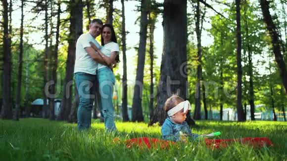 小女孩坐在草地上的毯子上父母远远地看着她视频的预览图