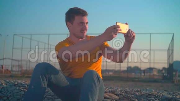 春天在海边穿着橙色T恤和牛仔裤的年轻人他在电话里拍了张照片视频的预览图