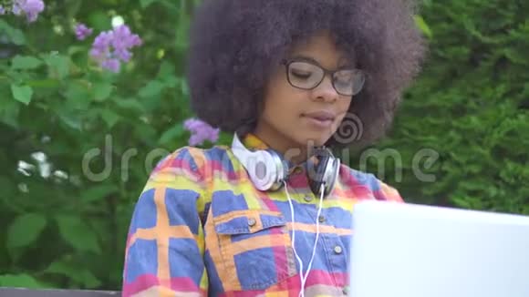 有非洲发型的美国黑人妇女肖像使用笔记本电脑坐在街上的长凳上视频的预览图