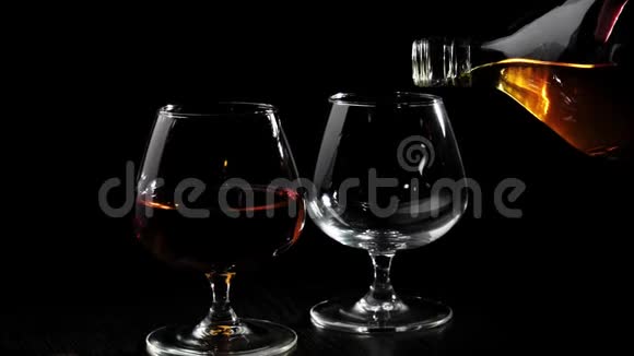 豪华白兰地手把金白兰地从一个圆形的瓶子里倒入一个玻璃杯里放在旋转的黑色桌子上靠近玻璃杯和白兰地视频的预览图
